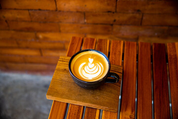 Cup of cappuccino with latte art on wooden background. Beautiful foam, wooden desk and bricks wall.