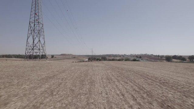 Drone fly over a female shepherd with sheeps in a remote desert area, under large power poles, near a highway, dry land without crops, push in shot(D-LOG)