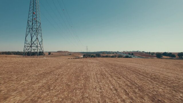 Drone fly over a female shepherd with sheeps in a remote desert area, under large power poles, near a highway, dry land without crops, push in shot