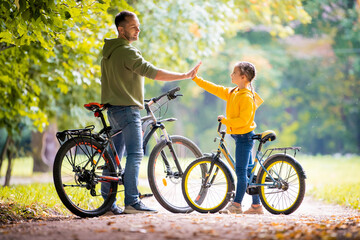 Fototapeta premium Happy father and daughter walk with bicycles in the autumn park on a sunny day.