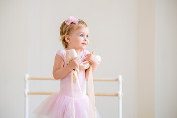 Portrait of a cute blue-eyed baby ballerina in pink hugging pointe shoes.