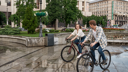 Obraz premium Smiling couple riding bicycles in city after rain