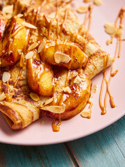 Close up of crepes on a pink plate with cooked apples, almonds and caramel