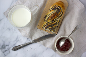 Freshly baked homemade sweet bun with jam and transparent glass of milk for breakfast