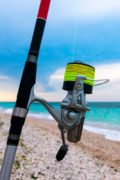 Vertical shot of fishing reel with green fishing line on the seashore. Sea fishing.