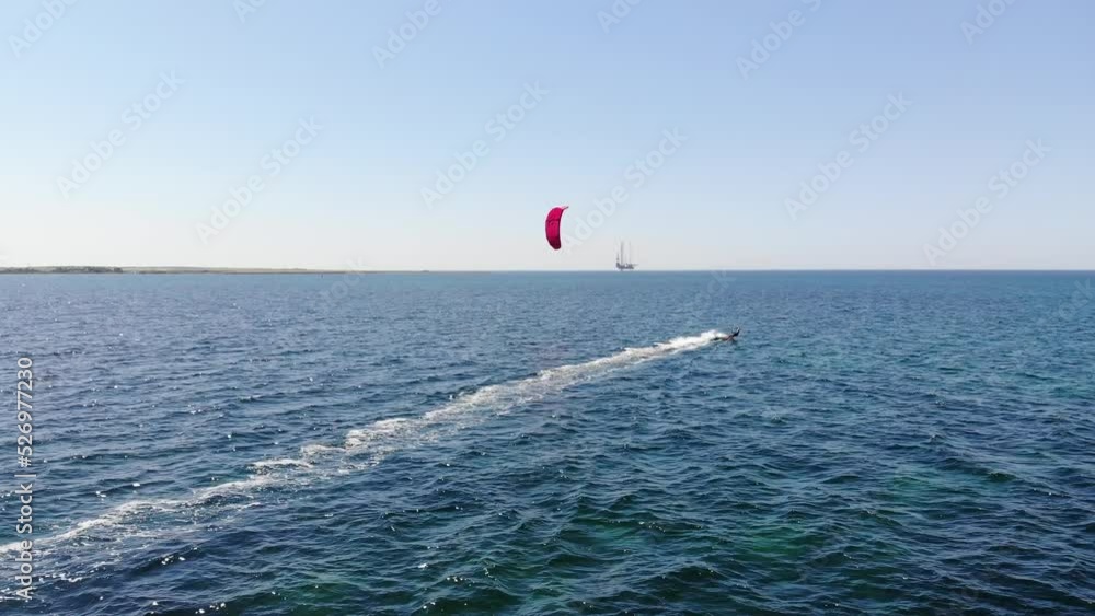 Wall mural Aerial view of a young female athlete on a kitesurf ride tack in the open sea on a sunny day. Kitesurfing and extreme water sports