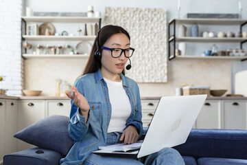 Young asian freelancer woman working remotely from home using headset and laptop for video call...