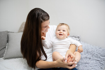 Fototapeta na wymiar pretty young and happy mother with dark hair, white t-shirt, blue pants is cuddling in bed with her 7 months old son with blue eyes