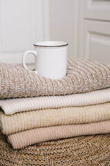 Fototapeta na wymiar A cup of hot coffee with milk on a stack of knitted clothes. Autumn mood. The concept of home comfort, cozy mood and winter morning. Hygge. Vertical photo.