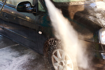 close-up of a jet of water from a sprayer washes a car at a self-service car wash