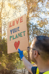 Hombre voluntario levantando una pancarta con el mensaje de ama tu planeta, en la montaña en un...