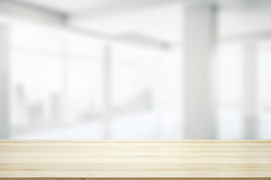 Blank wooden desktop with empty space on modern office interior with large window background, closeup, mock up