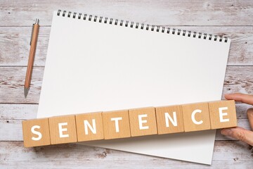 SENTENCEと書かれたブロック、ノート、ペン、手
