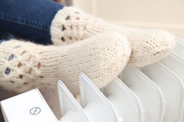 Heating season, woman warms her legs with heater