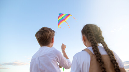 A girl and a boy launch bright kite into the sky, a view from the back.
