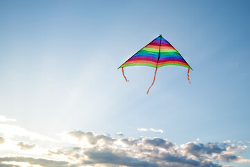 A kite flies sky with clouds, clouds and sun rays.