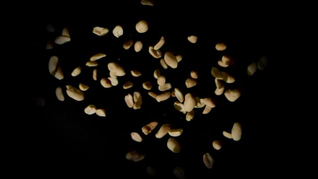 Static shot of a pile of shelled peanuts suddenly exploding outward then transiting into slow motion then falling to the ground on a black background