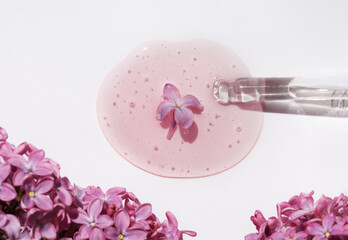 Closeup of pipette with serum, oil, gel with lilac flowers on white background. Skin care, natural beauty products presentation concept. Macro. Romantic floral composition. Front view, high angle shot