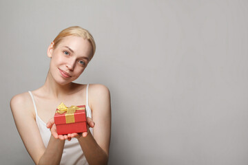 Cheerful adorable young woman holding red gift box with golden ribbon on white background, beauty portrait