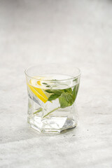 Morning beverage - a glass of lemon water with fresh mint on grey background, space for text