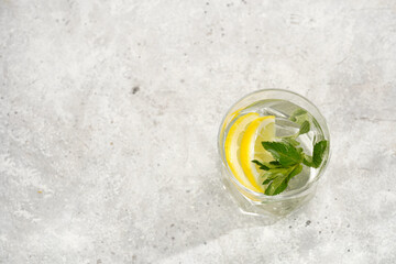 Morning beverage - a glass of lemon water with fresh mint on grey background, space for text