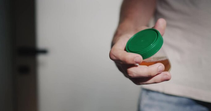 A man stands at the toilet door with a jar for urine tests. Health problem and urology concept