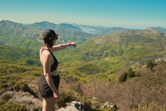 Young woman pointing out a mountainous landscape in Asturias, Spain. Pe&ntilde;a Mea trail.