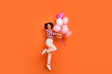 Full length body size view of attractive cheery girl jumping with helium balls rest event isolated on bright orange color background