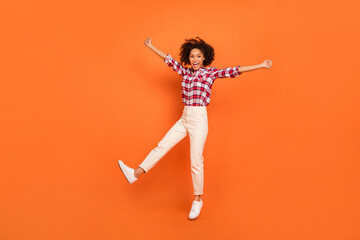 Photo of cute excited lady dressed checkered shirt jumping high rising fists isolated orange color background