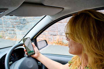 Woman using phone whilst driving. Picture of mature lady looking at her mobile phone in her car on the road. 
Risking breaking the law and dangerous driving in the UK