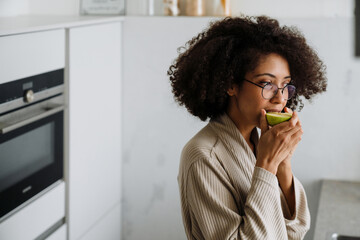 African american young woman with curly hairstyle eating apple at home