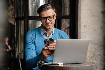 Adult handsome man in blue sweater and glasses using phone