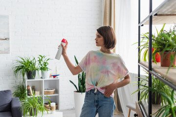Young woman spraying air freshener while standing in living room.