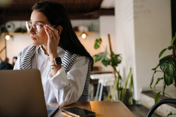 White woman in earphones working with laptop while sitting at cafe