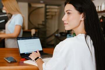 White brunette woman working with laptop while sitting in cafe