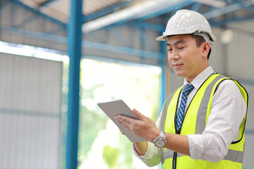 Architect or engineering man and worker standing and checking large warehouse with tablet. Asian business manager looking in future with warehouse building background.