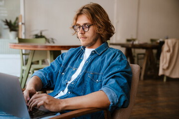 Young handsome long-haired calm man in glasses and jeans shirt