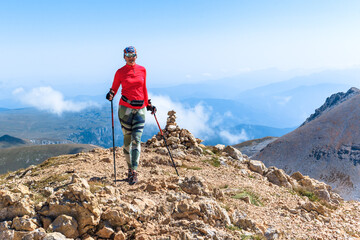 Obraz premium a female climber conquers the peak against the background of the blue sky enters the mountain with trekking poles