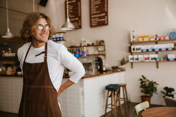 Portrait of young smiling long-haired man in apron and glasses