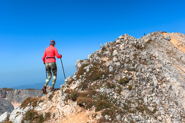 Naklejka premium a female climber conquers the peak against the background of the blue sky enters the mountain with trekking poles