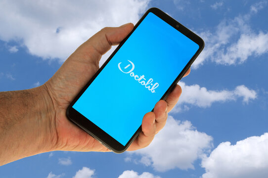 Vannes, France, 27 août 2022 : Application Doctolib sur un smartphone tenu en main en gros plan sur fond avec un ciel et des nuages