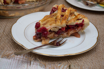 Apple Cranberry pie slice on burlap cloth, wooden white table