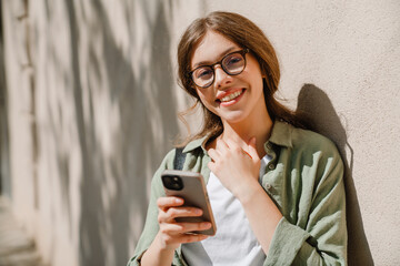 Fototapeta premium Young beautiful smiling woman in glasses holding phone touching neck