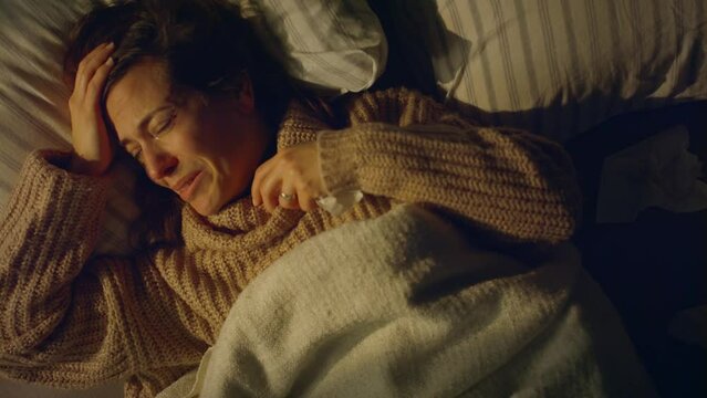 Sad woman suffering from depression lying in bed in night.