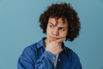 Fototapeta na wymiar Curly young man wearing shirt holding his chin while looking aside