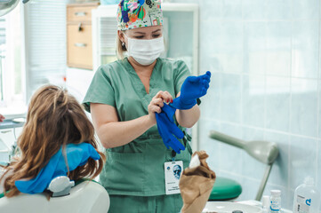 female dentist in gloves mask and cap with tools in hands the patient lies on the chair treatment dental office healthy teeth self care puts on hygiene gloves