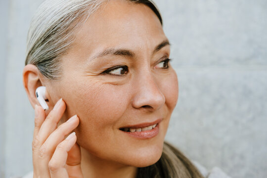 Asian mature woman in earphones laughing while listening music