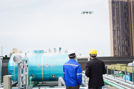 Professional Asian civil engineers using the unmanned aerial vehicle or UAV - drone for inspecting the building structure.