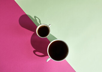 A minimal composition made of two coffee cups on a pink and green background. Coffee culture concept. Creative design. Contrast colors palette. Flat lay. Copy space.