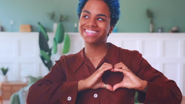 Young compassionate African American woman makes heart out of fingers showing kindness and love for people calls for volunteering and helping charitable foundations standing in living room